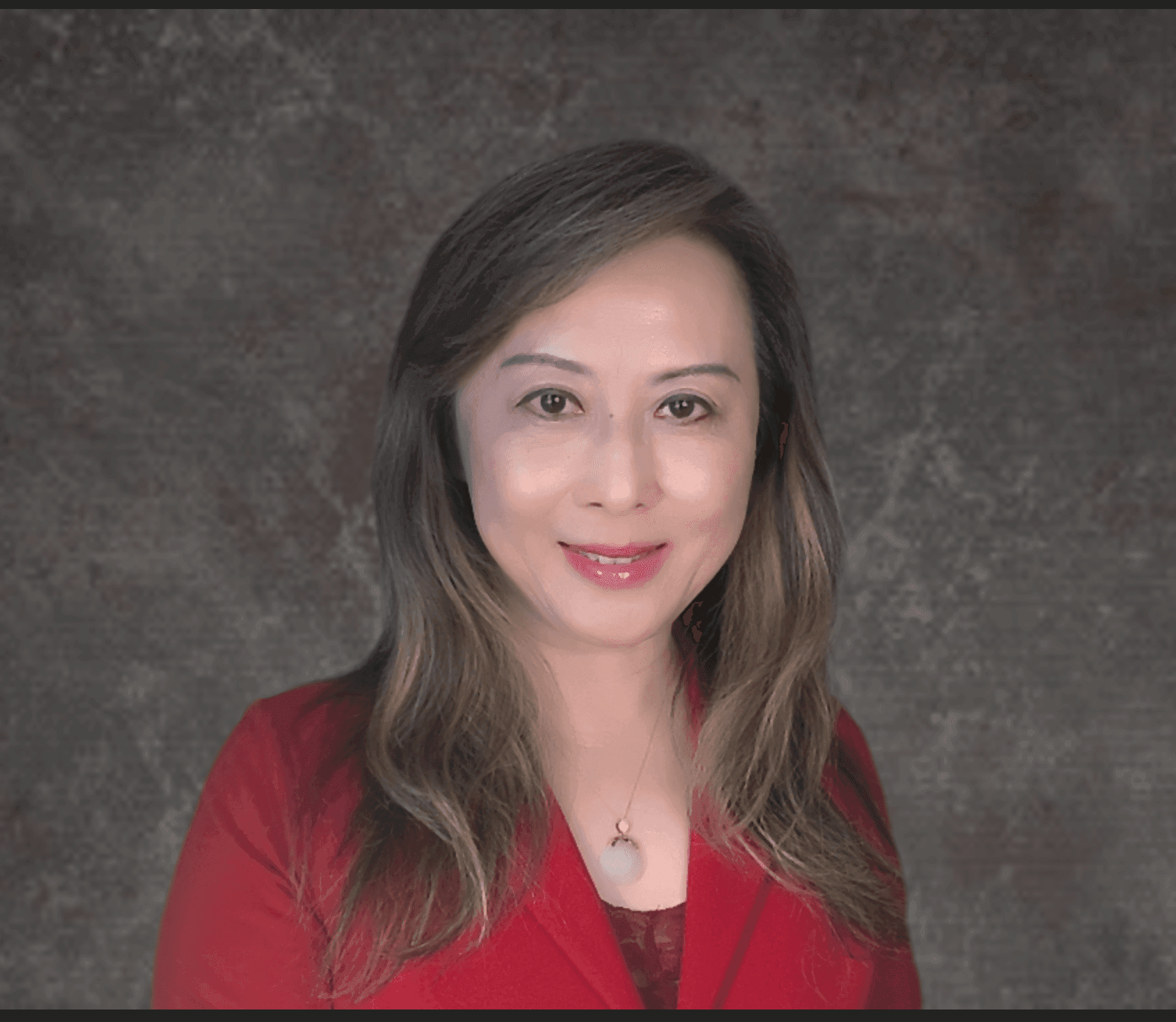 Person wearing a red blazer with long hair, smiling against a textured gray background.